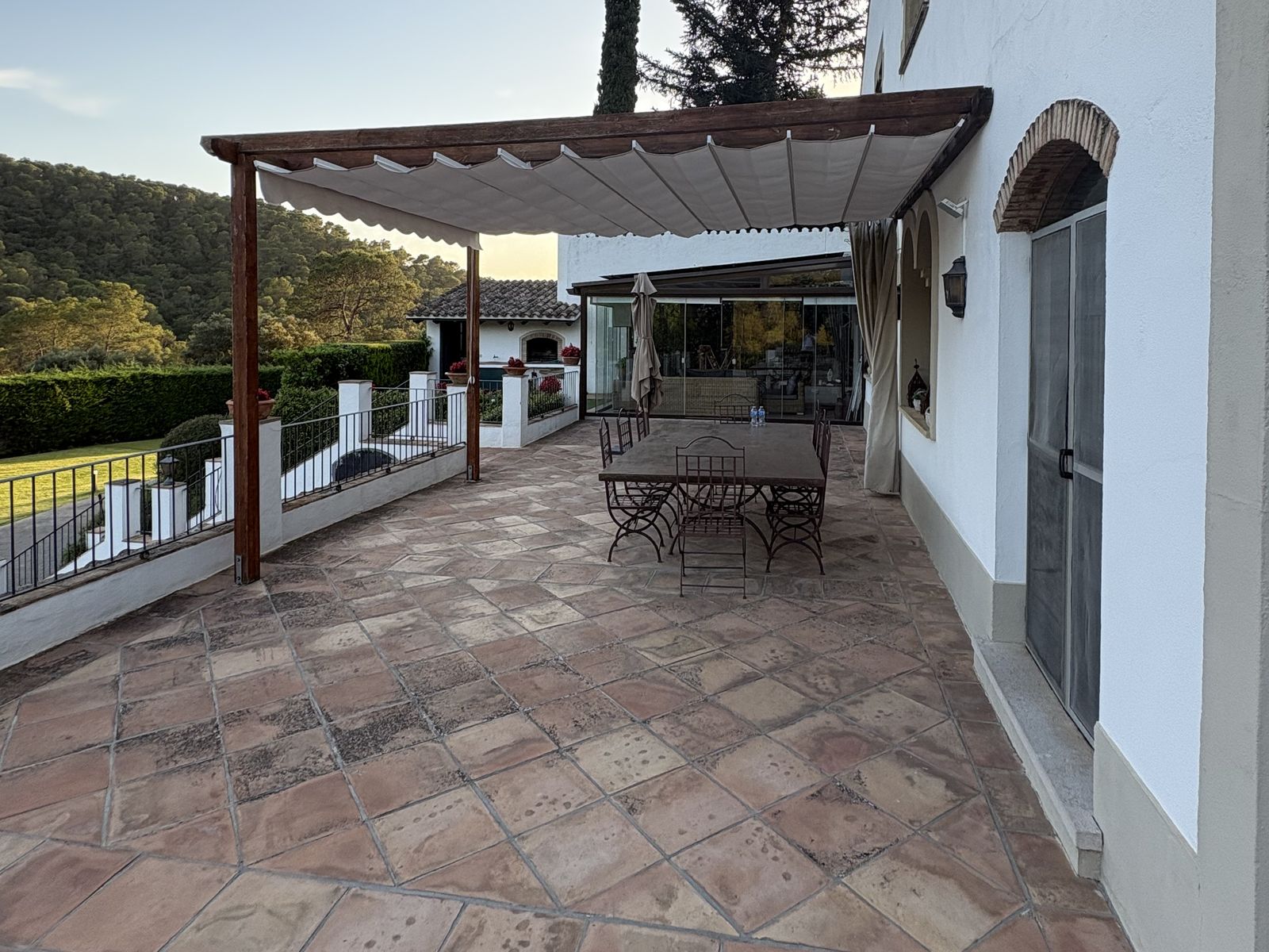 Toldo corredero con lona nueva extendido bajo la pérgola de madera, con la terraza en sombra al atardecer