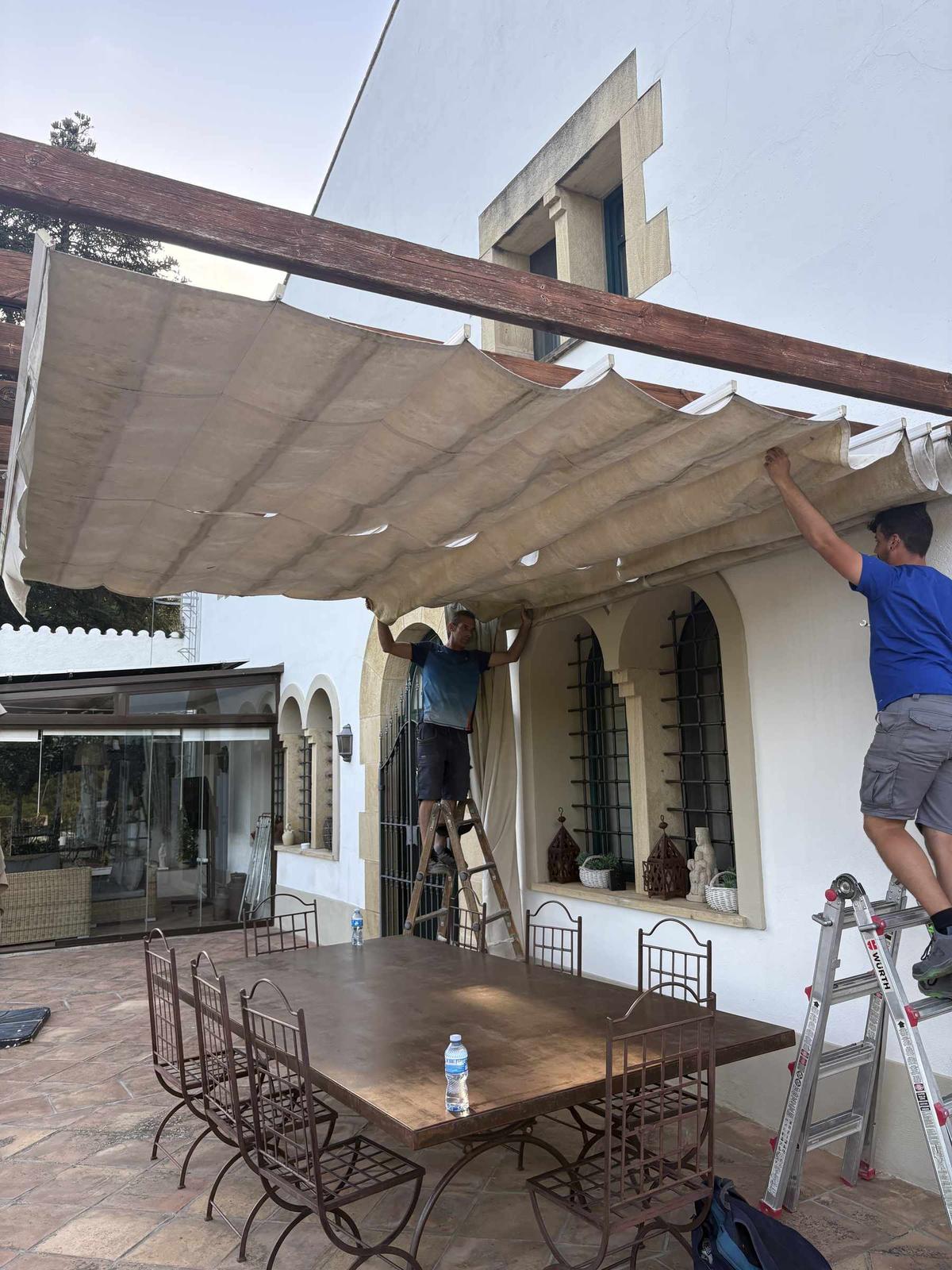 Dos operarios de COPERSE desmontando la lona antigua del toldo corredero bajo la pérgola de madera