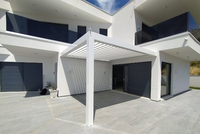 Pérgola bioclimática SEESKY-BIO con portería, apoyada en pilares y en la fachada de la vivienda (imagen del fabricante)