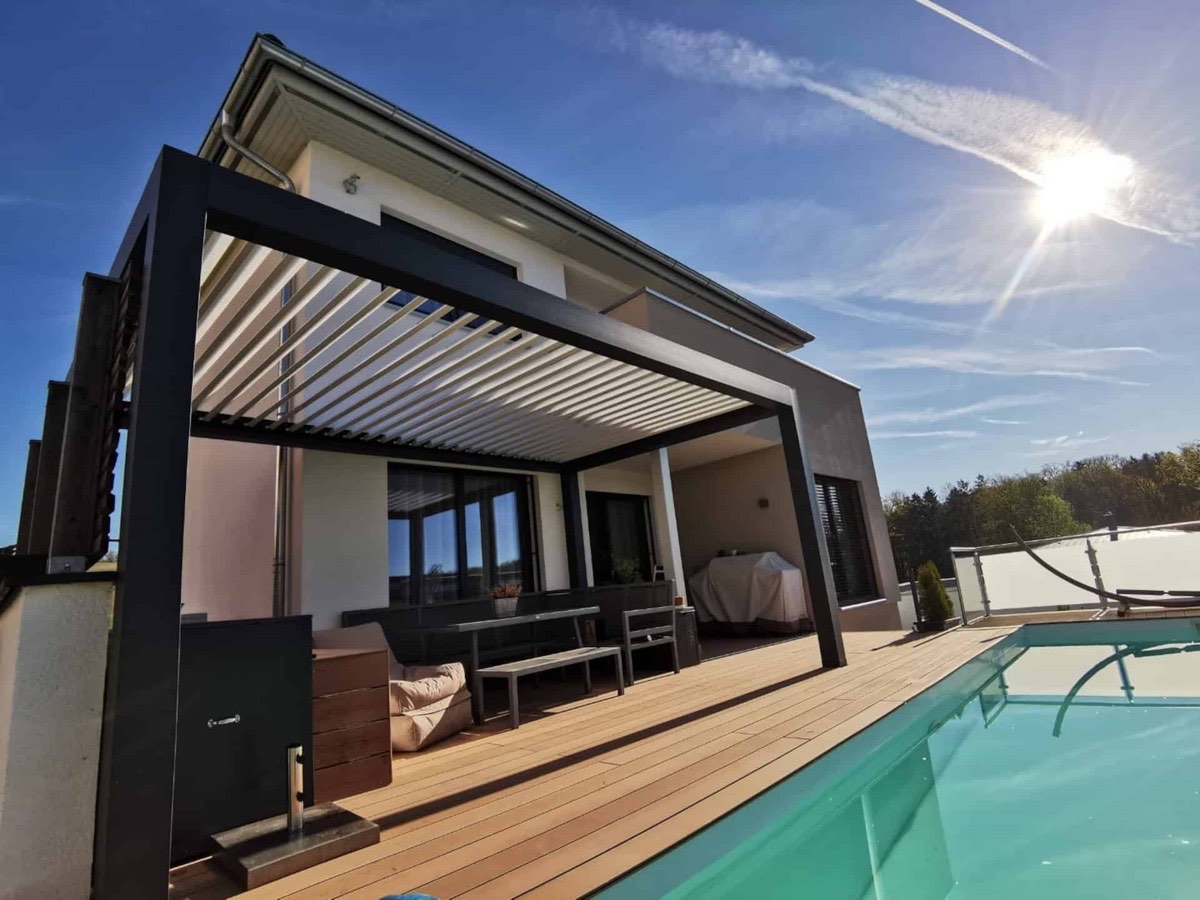 Sol entrando entre las lamas abiertas de una pérgola bioclimática SEESKY-BIO junto a una piscina (imagen del fabricante)