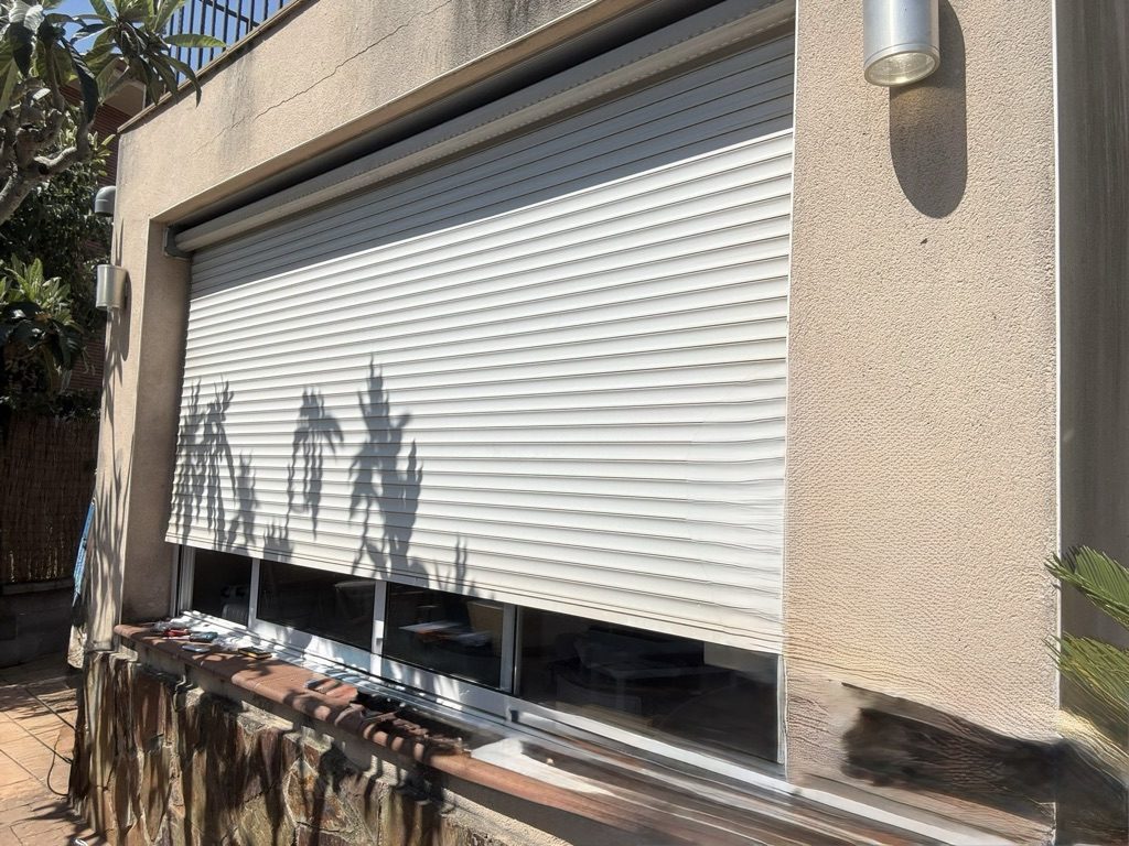 Persiana blanca recién instalada y bajada en la fachada de una vivienda, un día soleado