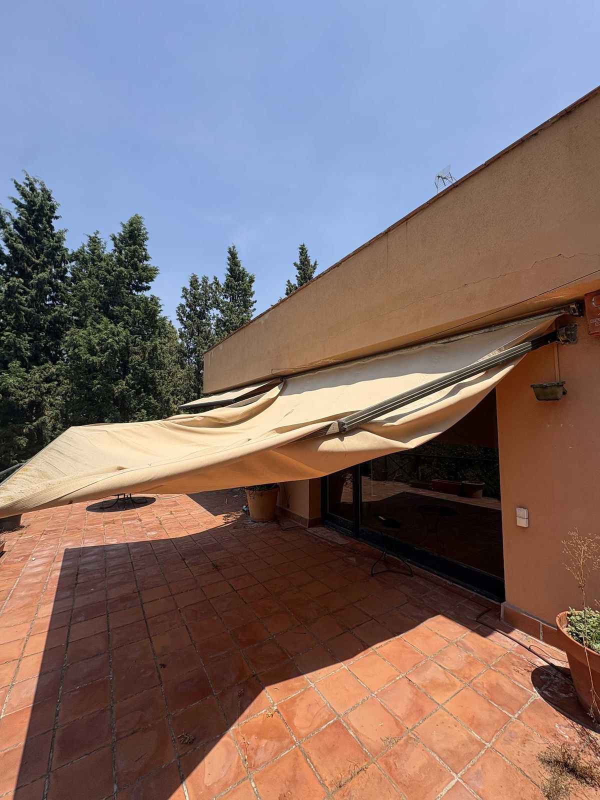 Toldo con la lona desprendida y descolgada sobre una terraza, pendiente de reparación