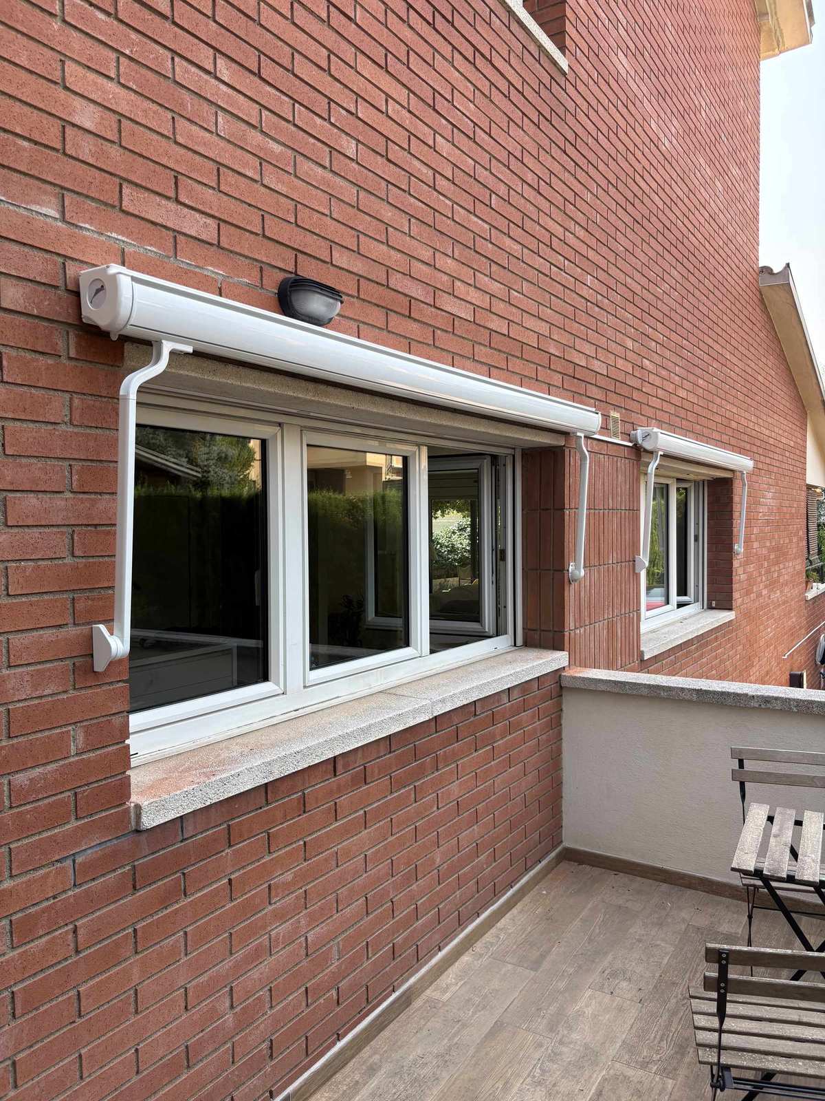 Dos toldos de cofre recogidos sobre las ventanas de una fachada de ladrillo